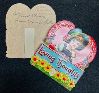 Photograph of a historical valentine, showing the front and inside. The front has a colourful illustration of a child in a bobnnet in front of a heart, standing behind a sign that says 'loving thoughts' with flowers. The inside is inscribed To Miss Oliver from Merry Gillian 